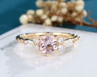 May include: A delicate gold engagement ring with a round pink morganite center stone surrounded by smaller diamonds. The ring has a twisted band and a floral design.