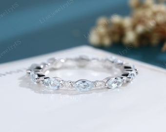 May include: A delicate eternity band featuring a row of marquise-shaped aquamarine gemstones set in a white gold band. The aquamarine stones are surrounded by smaller round diamonds.