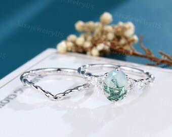 Peut inclure: Une bague de fiançailles en argent avec une pierre ovale en agate verte et de petits accents de diamants. La bague est sur un fond blanc.