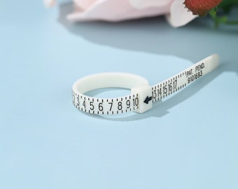 May include: White plastic ring sizer with black markings for measuring ring sizes from 2 to 10. The sizer has a flexible band and a ruler with markings from 13 to 17. The ruler also has the text "PAT. PEND. 9101693".