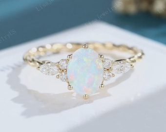 Op de afbeelding: Een gouden ring met een centrale ovale iriserende opaal, geflankeerd door twee marquise-geslepen heldere stenen en twee kleinere ronde heldere stenen aan elke kant. De ringband heeft een gedraaide, touwachtige textuur voor een gedetailleerd uiterlijk.