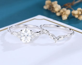 May include: A silver-toned engagement ring set featuring a central oval-cut stone flanked by marquise-cut stones, paired with a matching V-shaped wedding band adorned with smaller marquise-cut stones along the thin, polished metal band.