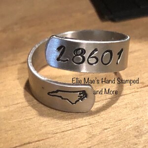 May include: A silver ring with the number "18601" engraved on it. The ring also features a silhouette of the state of North Carolina. The ring is made by Ellie Mae's Hand Stamped and More.