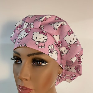 Puede incluir: Un gorro quirúrgico rosa con un estampado repetido del personaje Hello Kitty en blanco y rosa. El gorro está diseñado con una corona fruncida y un ajuste cómodo, adecuado para profesionales médicos o cualquier persona que busque un cubrecabezas divertido y funcional.