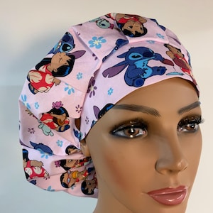 May include: A pink scrub cap featuring cartoon characters Lilo and Stitch, with blue and white floral accents. The cap is made of a soft fabric and is designed to fit comfortably. The cap is a fun and functional accessory for healthcare professionals.