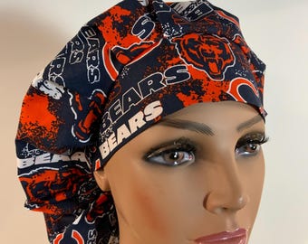 May include: A navy blue and orange patterned scrub cap featuring the text "BEARS" and a bear logo. The cap is designed with a gathered back and a wide band. The fabric has a repeating pattern of the team's logo and name.
