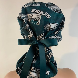 May include: Green and white surgical scrub hat with a Philadelphia Eagles pattern. The hat has a green ribbon tied at the back.