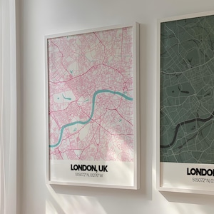 May include: Two framed London, UK map prints. One map is pink with a blue river, the other is green. Both have white frames and the text "LONDON, UK" at the bottom. The prints are hanging on a white wall above a pink armchair.