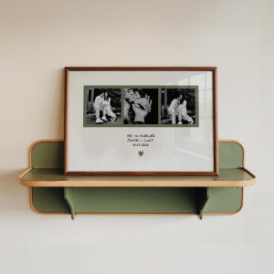 Può includere: Una stampa incorniciata con tre fotografie in bianco e nero. La cornice marrone contiene il testo "YES TO FOREVER JAMES + LUCY 18.03.2024" e un cuore verde. La stampa è esposta su una mensola verde e color legno, fissata a un muro bianco.
