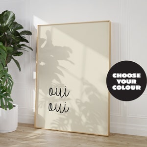 Puede incluir: Una impresi&oacute;n enmarcada con la palabra "oui" escrita dos veces en cursiva negra sobre un fondo beige claro. La impresi&oacute;n est&aacute; en un marco dorado y est&aacute; colgada en una pared blanca. Un c&iacute;rculo negro con el texto "CHOOSE YOUR COLOUR" est&aacute; en la esquina inferior derecha de la imagen.
