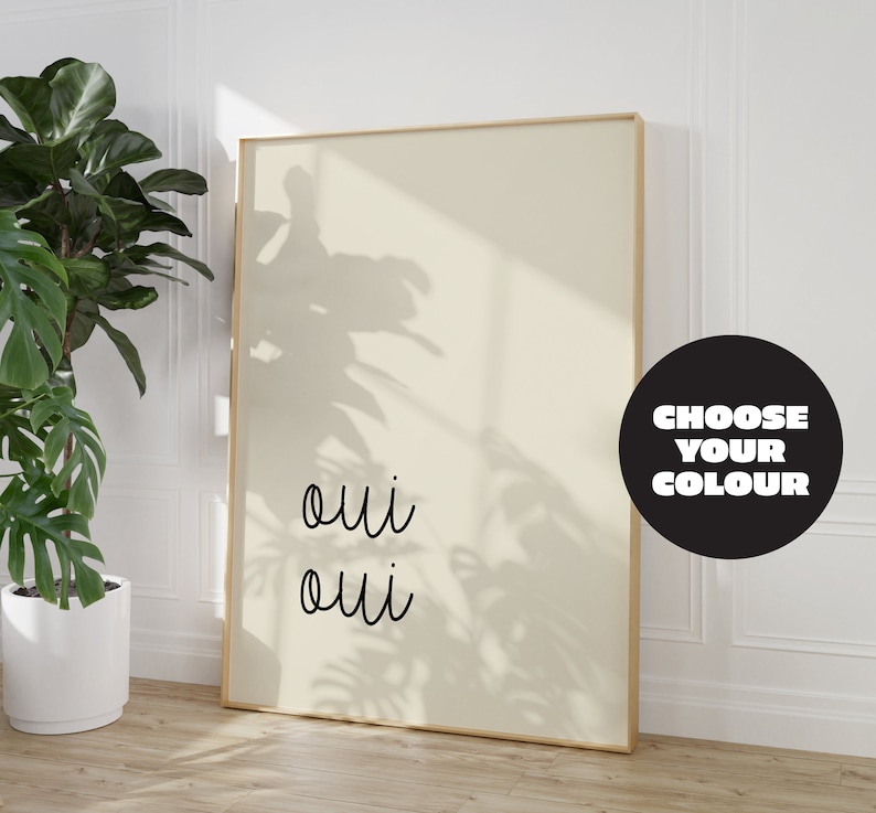 Puede incluir: Una impresi&oacute;n enmarcada con la palabra "oui" escrita dos veces en cursiva negra sobre un fondo beige claro. La impresi&oacute;n est&aacute; en un marco dorado y est&aacute; colgada en una pared blanca. Un c&iacute;rculo negro con el texto "CHOOSE YOUR COLOUR" est&aacute; en la esquina inferior derecha de la imagen.