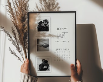 以下が含まれることがあります： 3つの小さな白黒写真が入った黒いフレームプリント。プリントには「HAPPY first anniversary」の文字と2025年7月のカレンダーが含まれています。プリントは人が持っています。