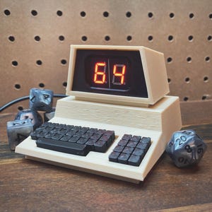 May include: A vintage-style computer with a red digital display showing the number 84. The computer has a black keyboard and is surrounded by gray dice.