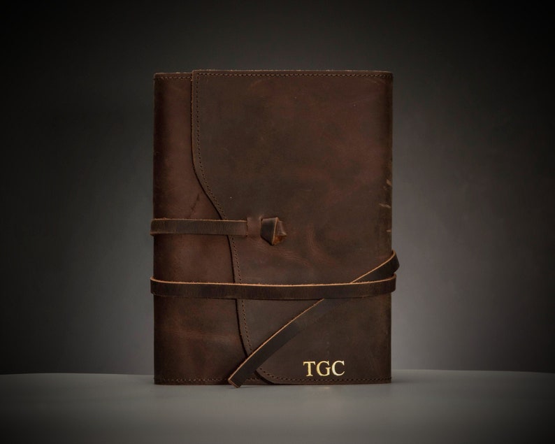 May include: A brown leather journal with a strap closure and the initials "TGC" embossed in gold on the front cover.