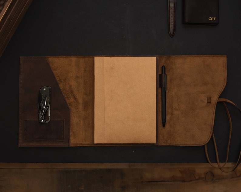 May include: A brown leather journal with a pen and a multi-tool in the pockets. The journal has a flap that closes with a strap.