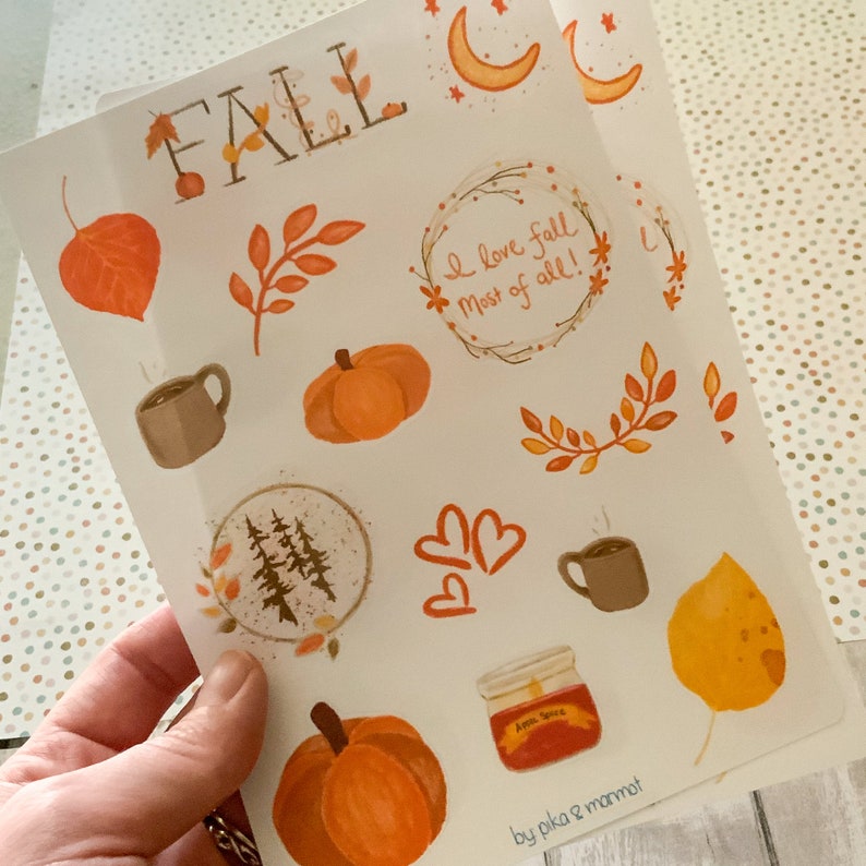 May include: A sheet of fall-themed stickers with illustrations of pumpkins, leaves, coffee mugs, a jar of apple spice, and a forest scene. The text "FALL" is at the top of the sheet, and the text "I love fall most of all!" is in a wreath with leaves. The text "by pika & mammot" is at the bottom of the sheet.