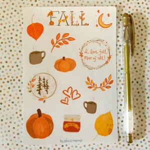 May include: A sheet of fall-themed stickers featuring illustrations of pumpkins, leaves, a coffee mug, a candle, a moon, and a forest. The stickers also include the words "Fall" and "I love fall most of all!" The sheet is white with a light brown background and is signed "by pika & mammot".