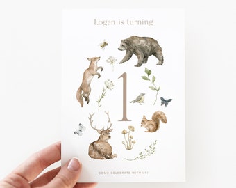 May include: A woodland-themed first birthday invitation with a large number "1" surrounded by animals like a bear, fox, deer, squirrel, and birds. The text "Logan is turning 1" and "Come celebrate with us!" is printed on the invitation.