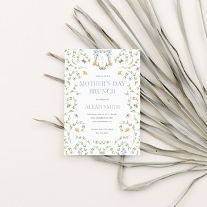 Pu&ograve; includere: Un invito bianco con un bordo floreale e il testo "Mother's Day Brunch" in lettere blu. L'invito &egrave; per un brunch in onore di Aleah Smith sabato 23 maggio alle 11:30 al 605 Celebration Way, Santa Barbara, CA. Il numero di telefono 805.385.3415 &egrave; incluso.