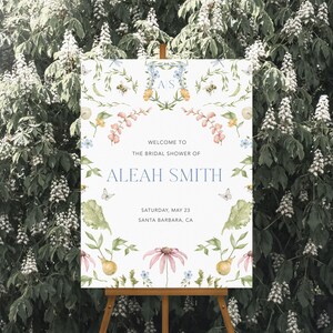 May include: A white bridal shower sign with a floral design and the text "Welcome to the bridal shower of Aleah Smith, Saturday, May 23, Santa Barbara, CA".