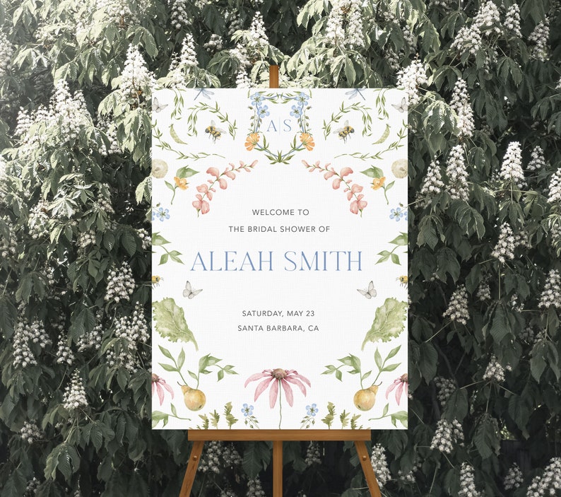 May include: A white bridal shower sign with a floral design and the text "Welcome to the bridal shower of Aleah Smith, Saturday, May 23, Santa Barbara, CA".