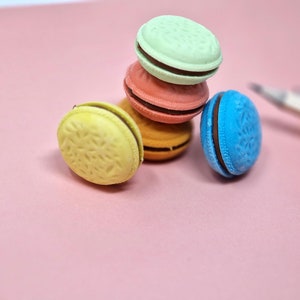 Könnte beinhalten: Ein Stapel von vier bunten Macarons auf einer rosa Oberfläche. Die Macarons sind mit einem Muster verziert und haben eine Schokoladenfüllung.