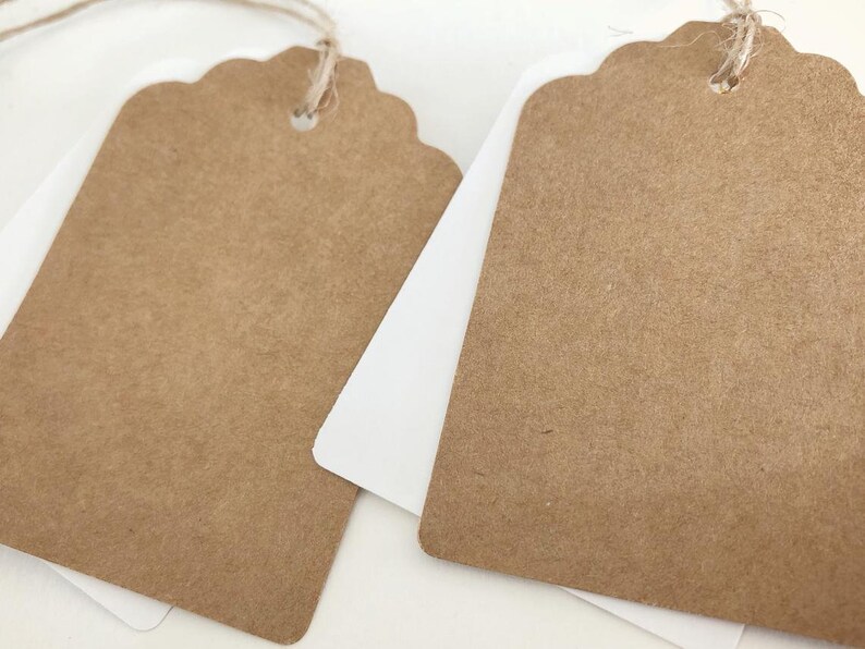 May include: Two brown paper gift tags with scalloped edges and a hole punched at the top. The tags are tied with twine.