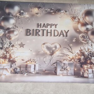 May include: A silver and white birthday backdrop with balloons, gifts, and floral arrangements. The words "HAPPY BIRTHDAY" are displayed. The backdrop has a soft, dreamy aesthetic, ideal for celebrations.