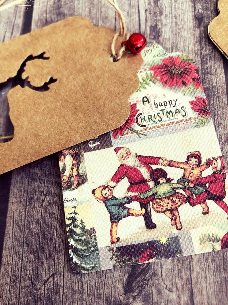 K&ouml;nnte beinhalten: Ein Weihnachtsgeschenkanh&auml;nger im Vintage-Stil mit braunem Papierhintergrund und einem ausgeschnittenen Rentiermotiv. Die Vorderseite des Anh&auml;ngers zeigt eine farbenfrohe Illustration von Weihnachtsmann und Kindern, die sich im Kreis an den H&auml;nden halten, mit dem Text "A happy Christmas" in einer dekorativen Schrift.