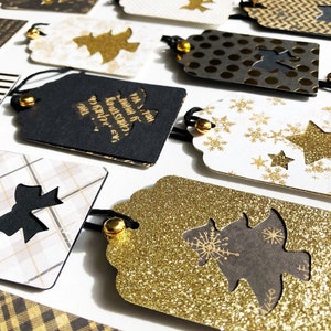 Pu&ograve; includere: Una collezione di etichette regalo di Natale nere e dorate con vari disegni, tra cui fiocchi di neve, stelle, fiocchi e alberi di Natale. Le etichette sono realizzate in carta e hanno una finitura glitter.