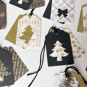 Pu&ograve; includere: Una collezione di etichette regalo di Natale con una variet&agrave; di design. Le etichette sono realizzate in carta bianca e nera con accenti di glitter dorati. Alcune delle etichette presentano un design ritagliato di un albero di Natale. Il testo sulle etichette recita "Deck the halls very merry Christmas".