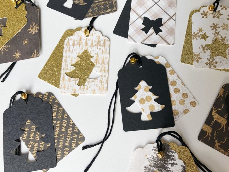 Pu&ograve; includere: Una collezione di etichette regalo di Natale con una variet&agrave; di design. Le etichette sono realizzate in carta bianca e nera con accenti di glitter dorati. Alcune delle etichette presentano un design ritagliato di un albero di Natale. Il testo sulle etichette recita "Deck the halls very merry Christmas".