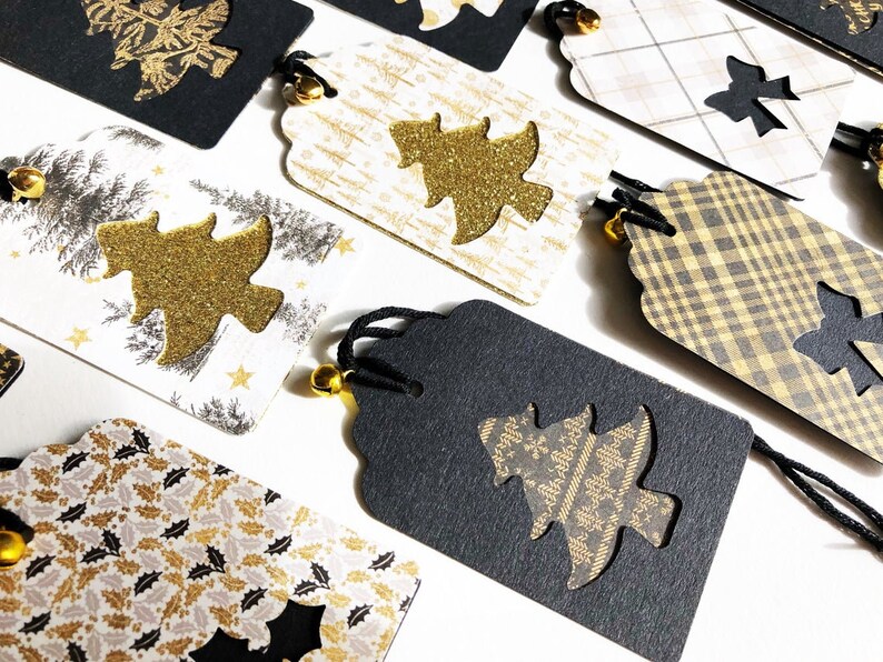 Pu&ograve; includere: Un set di otto etichette regalo di Natale con una variet&agrave; di motivi e design. Le etichette sono nere, bianche e dorate con una finitura scintillante. Ogni etichetta presenta un design ritagliato di un albero di Natale o di un fiocco. Le etichette sono legate con uno spago nero e hanno una piccola campana.