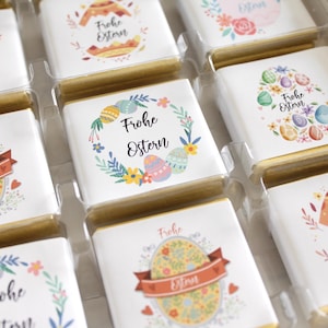 Könnte beinhalten: Sortiment kleiner, quadratischer, weißer Schokoladentafeln mit bunten Ostermotiven und dem Text "Frohe Ostern".