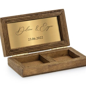 May include: A wooden ring box with a hinged lid and two compartments. The lid has a gold plaque with the inscription "Dilara & Ergin 23.06.2022".