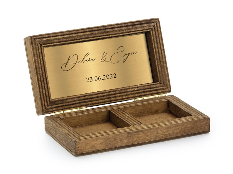 May include: A wooden ring box with a hinged lid and two compartments. The lid has a gold plaque with the inscription "Dilara & Ergin 23.06.2022".