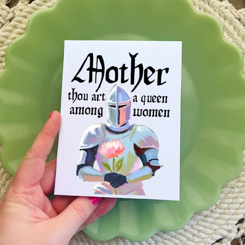 May include: A white card with black text that reads "Mother thou art a queen among women". The card features a painting of a knight in silver armor holding a pink flower.