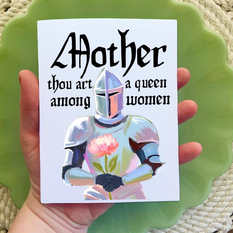 May include: A white card with a knight in armor holding a pink flower. The card has the text "Mother thou art a queen among women" in black.