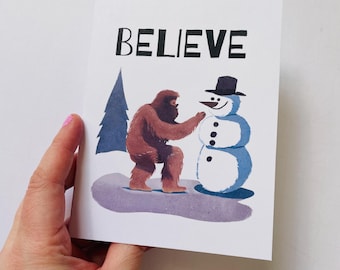Bigfoot Christmas Card: Watercolor Sasquatch Building Snowman