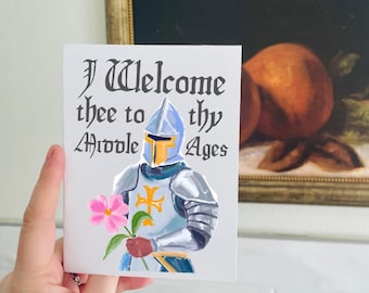 May include: A white card with a knight in silver armor holding a pink flower. The knight is wearing a helmet with a gold trim. The card has the text "I welcome thee to thy noble ages" in black.