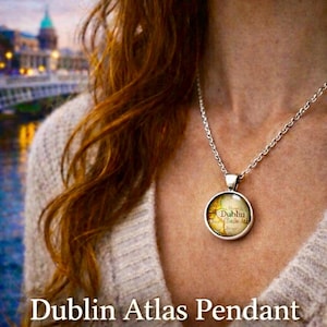 May include: A silver-toned pendant necklace featuring a circular charm with a vintage map of Dublin. The necklace is worn against a neutral-colored sweater. Text on the image reads "Dublin Atlas Pendant" and "Vintage Baile Átha Cliath Map Necklace."