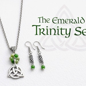 Pode incluir: O conjunto Emerald Trinity. Um colar prateado com um pendente de nó celta e detalhes de contas verdes, combinado com brincos pendurados a condizer. O conjunto apresenta o texto "The Emerald Trinity Set" em verde.