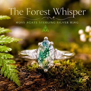 May include: A sterling silver ring featuring a marquise-cut moss agate centre stone flanked by two triangular-cut clear stones. The text "The Forest Whisper" and "MOSS AGATE STERLING SILVER RING" is printed above the ring in white lettering.