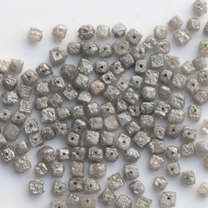 May include: A pile of small, gray, square-shaped diamonds. The diamonds are rough and have a matte finish.