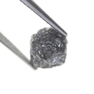 Pode incluir: Uma caneca de cer&acirc;mica branca com uma al&ccedil;a preta e o texto "But first, coffee" em preto, com uma fonte manuscrita. A caneca est&aacute; sobre uma superf&iacute;cie branca.