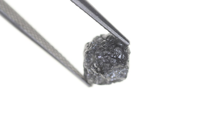 Pode incluir: Uma caneca de cer&acirc;mica branca com uma al&ccedil;a preta e o texto "But first, coffee" em preto, com uma fonte manuscrita. A caneca est&aacute; sobre uma superf&iacute;cie branca.