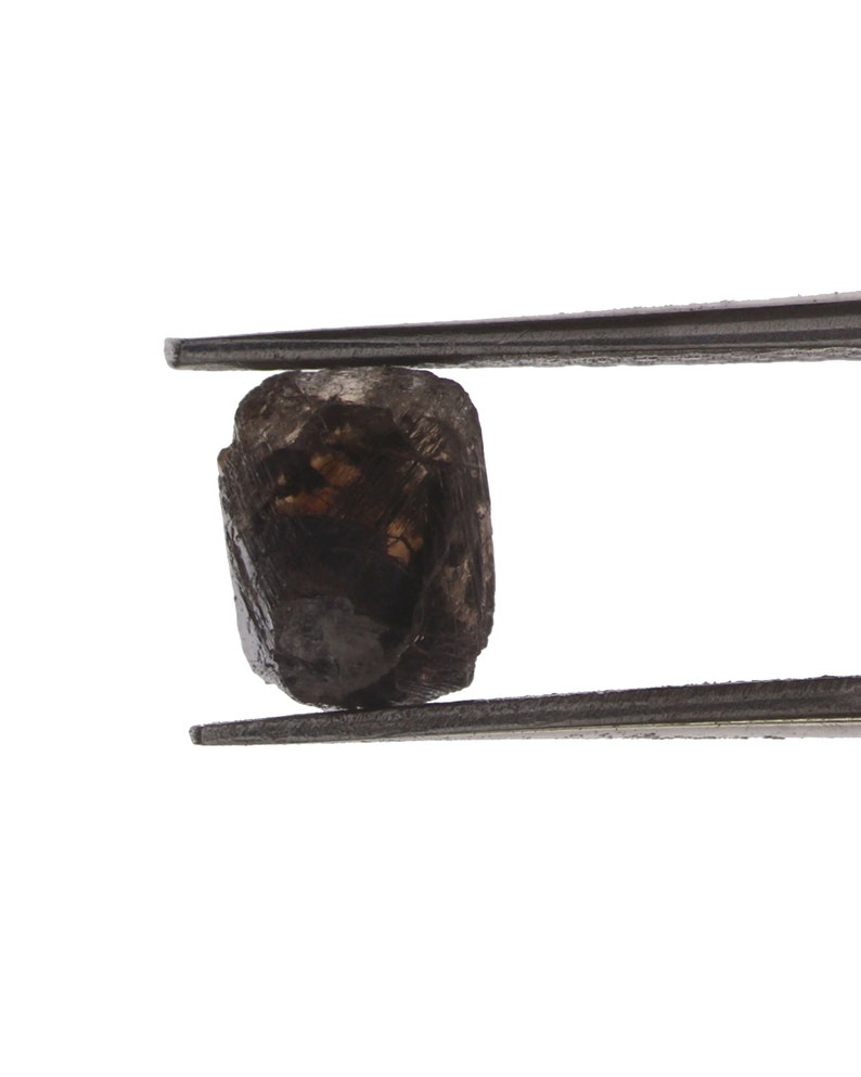 Puede incluir: Una piedra preciosa de color gris oscuro, rugosa y opaca, est&aacute; sujeta por unas pinzas. La piedra preciosa es un diamante en bruto.