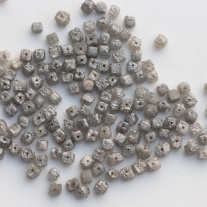 May include: A pile of small, gray, square-shaped diamonds with holes drilled through the center. The diamonds are rough and have a natural, unpolished look.