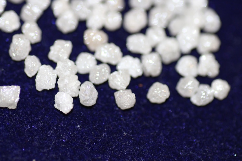 Op de afbeelding: Een close-up van een verzameling kleine, witte, ruwe diamanten op een donkerblauwe achtergrond.