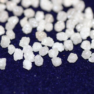 Op de afbeelding: Een close-up van een stapel kleine, witte, ruwe diamanten op een donkerblauw fluwelen oppervlak.